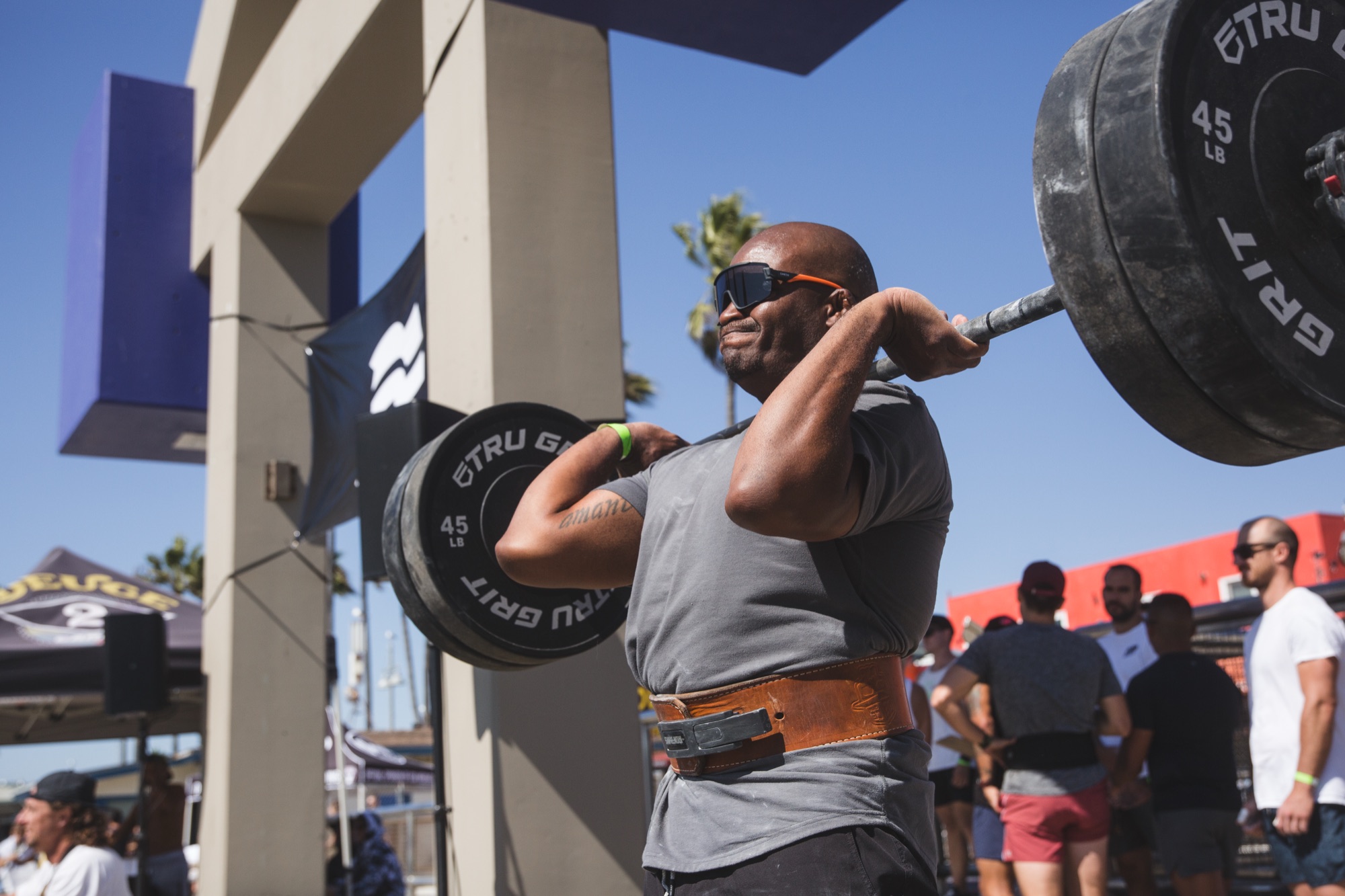 A lifter in shades racks a clean with a thick weight belt.