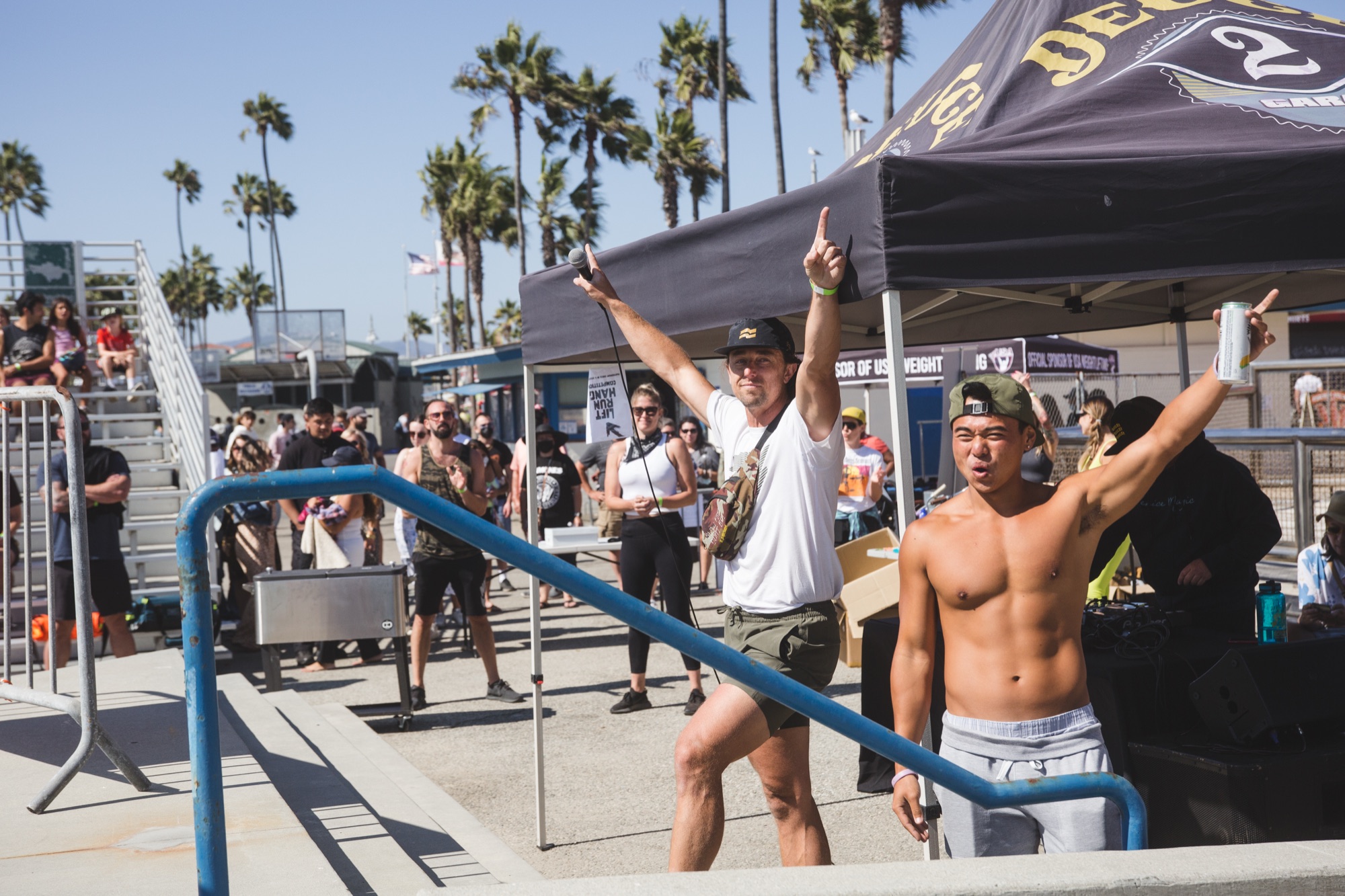 Two friends with arms up under the DEUCE tent at the boardwalk.