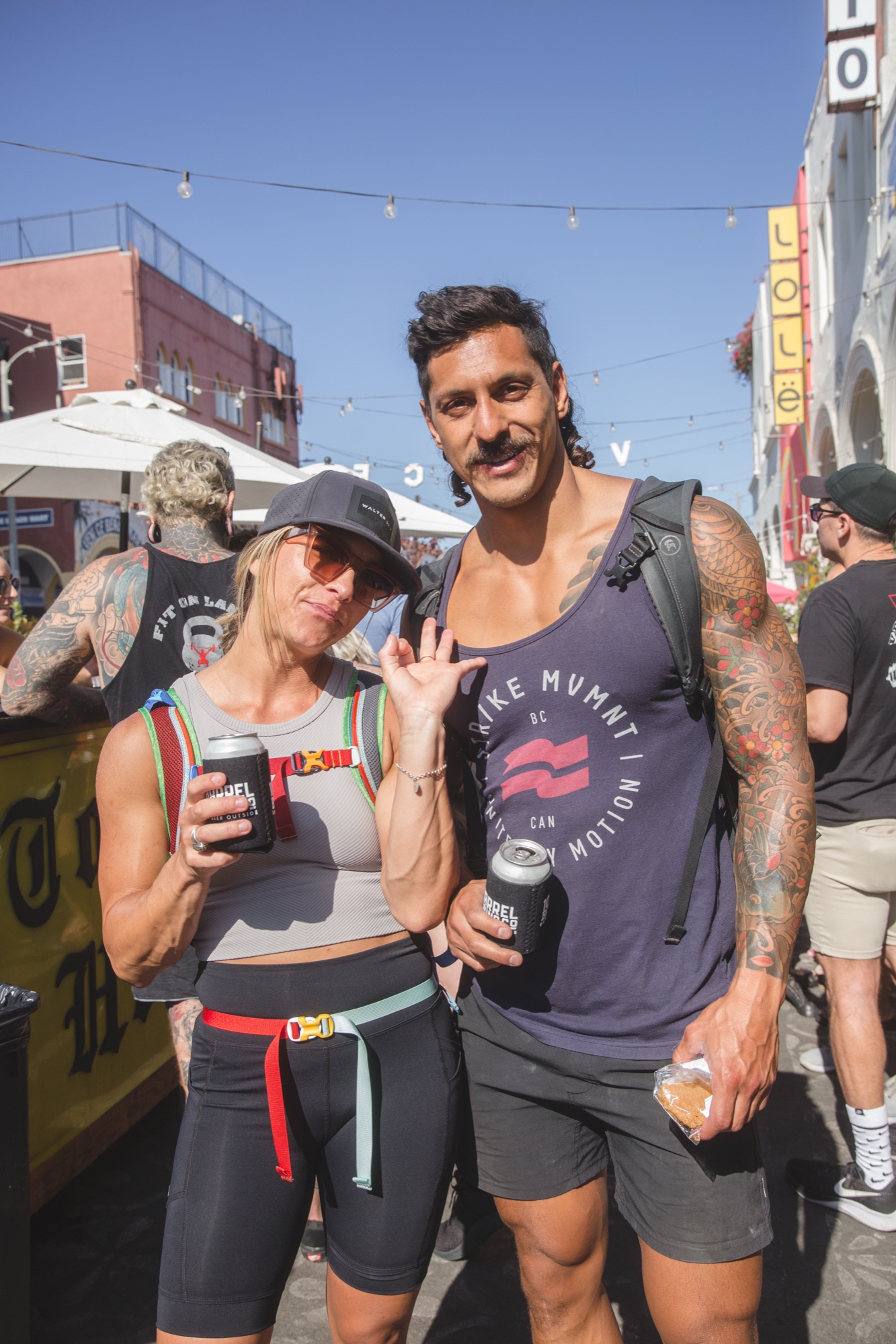 Two friends in STR/KE MVMNT gear holding cans at the beer garden.